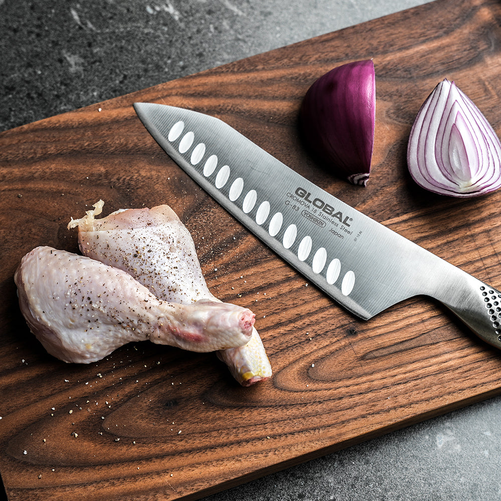 Cuchillo Global G-83 oriental sobre superficie de madera, detalle hoja alveolada