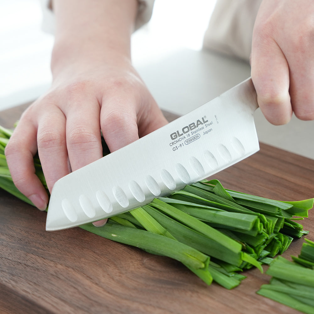 Cuchillo Global GS-91 vegetales alveolado sobre superficie de madera, detalle hoja